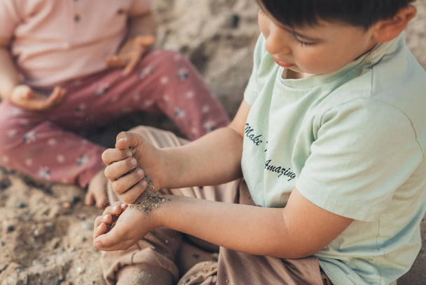 Két kaukázusi gyerek homokkal játszik és felfedezi a természetet, a falu kertjében ülve. Kertészkedés és fenntartható élet. Boldogság koncepció. Család - Fotó, kép
