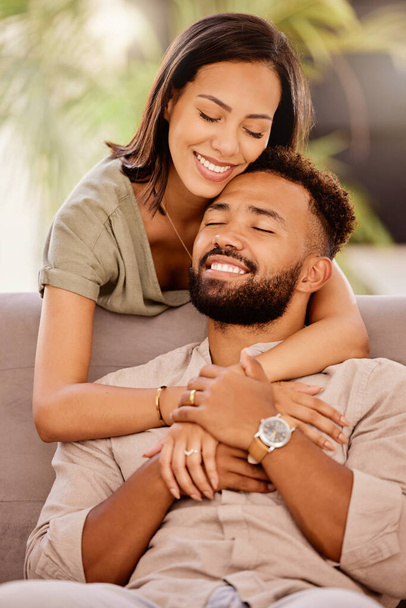 Happy, love and hug with a black couple on the sofa to relax in the living room of the home together. Smile, happy and hugging with a male and female bonding in the lounge of their house for romance. - Photo, Image