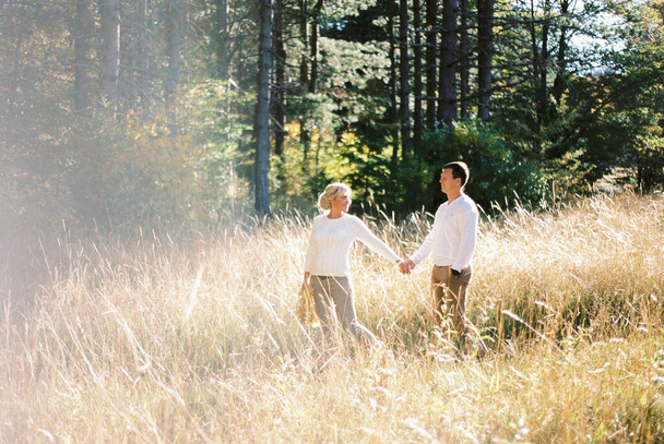 Mann und Frau stehen im hohen trockenen Gras auf einer Lichtung und halten Händchen. Hochwertiges Foto - Foto, Bild