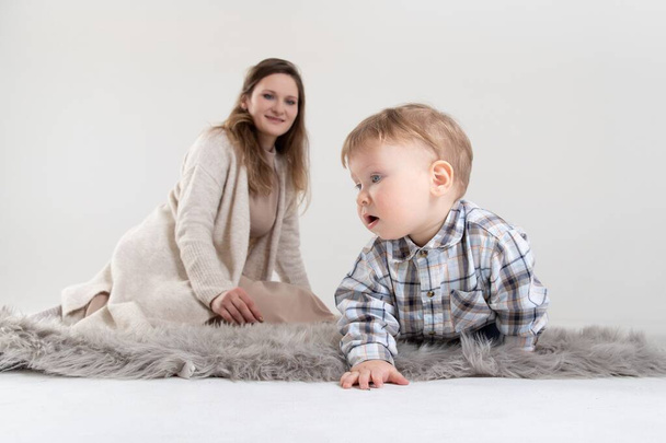 Studio portret rocznego dziecka czołgającego się po dywanie i oglądanego przez matkę. - Zdjęcie, obraz