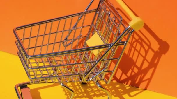 Hand add 20 dollar banknote Money in toy supermarket trolley shopping cart on yellow background. Sales Basket of US dollar bills. Minimum living wage Concept: loan, investment pension saving money - Footage, Video