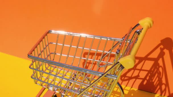 Hand duwen speelgoed supermarkt trolley met 100 dollar bankbiljet Geld in winkelwagen op gele achtergrond. Verkoopmand met US dollar biljetten. Minimaal leefbaar loon Concept: lening, pensioensparen - Video