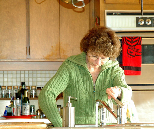 Dojrzałe kobieta senior pracy i sprzątanie lady w kuchni w pomieszczeniach. - Zdjęcie, obraz