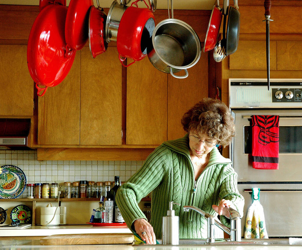 Dojrzałe kobieta senior pracy i sprzątanie lady w kuchni w pomieszczeniach. - Zdjęcie, obraz