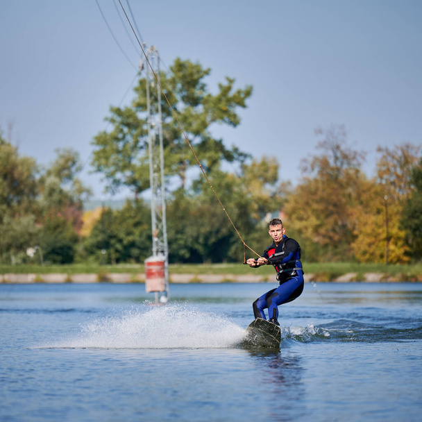 Um wakeboarder a surfar no lago. Surfista jovem se divertindo wakeboarding no parque a cabo. Desporto aquático, conceito de atividade ao ar livre. - Foto, Imagem