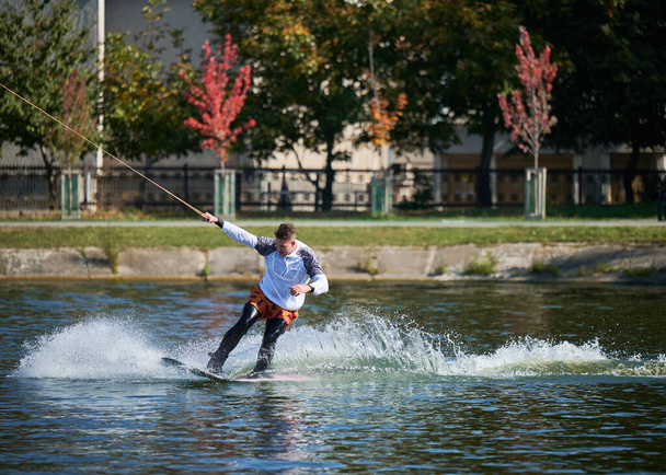 Um wakeboarder a surfar no lago. Surfista jovem se divertindo wakeboarding no parque a cabo. Desporto aquático, conceito de atividade ao ar livre. - Foto, Imagem