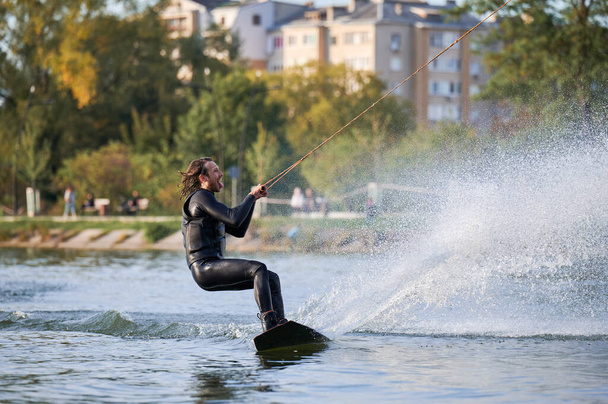 Wakeboarder making tricks while wakeboarding on lake. Young man surfer having fun wakesurfing in the cable park. Water sport, outdoor activity concept. - Photo, Image