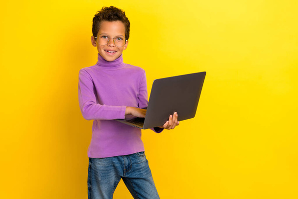 Portrait of cheerful smart schoolchild hols use wireless netbook isolated on yellow color background. - Zdjęcie, obraz