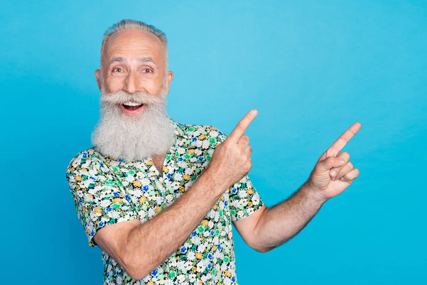 Photo of attractive cheerful retired guy wear flower print shirt pointing two fingers empty space isolated blue color background. - Foto, immagini