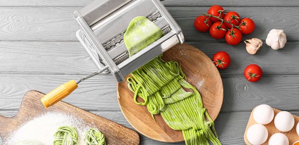 Pasta machine with green dough and ingredients on wooden background, top view - Photo, Image