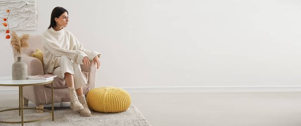 Nuori nainen istuu beige nojatuoli lähellä valoa seinään tilaa tekstiä - Valokuva, kuva