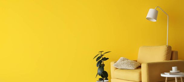 Interior da sala de estar com poltrona amarela, mesa, planta de sala e lâmpada perto da parede amarela com espaço para texto - Foto, Imagem