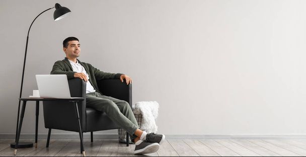 Nuori mies istuu mustassa nojatuolissa lähellä valoseinää, jossa on tilaa tekstille - Valokuva, kuva