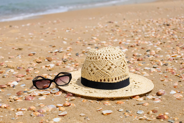 Стильная шляпа с солнцезащитными очками и ракушками на песке - Фото, изображение