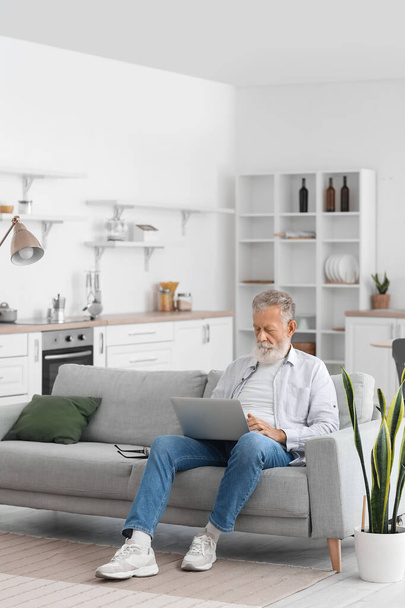 Senior bearded man using laptop on sofa in kitchen - Foto, Imagem