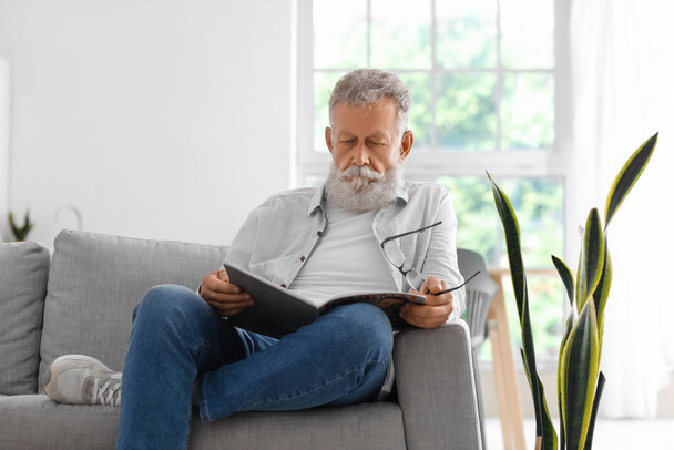 Älterer bärtiger Mann liest Magazin zu Hause auf dem Sofa - Foto, Bild