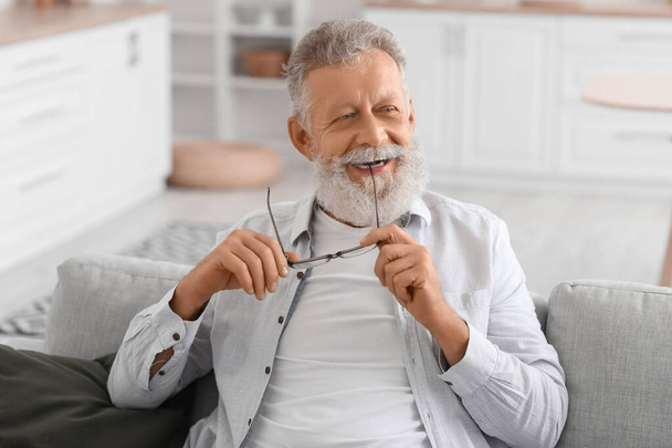 Старший бородатий чоловік з окулярами сидить на дивані на кухні
 - Фото, зображення