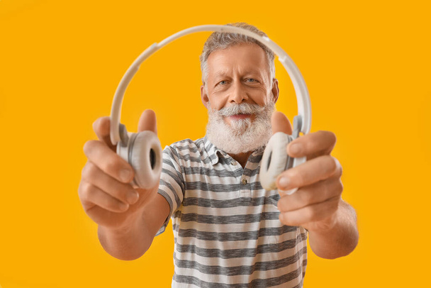 Senior bearded man with headphones on yellow background - Foto, Imagen