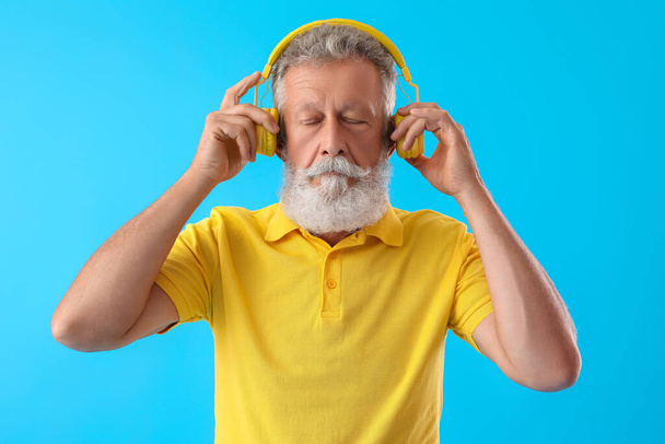Hombre barbudo mayor en auriculares sobre fondo azul - Foto, Imagen