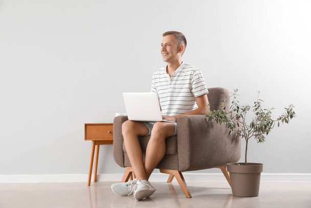 Young man using laptop in soft armchair near light wall - Foto, immagini