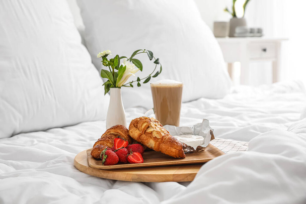 Tablett mit leckerem Frühstück, Kaffee und Blumen auf weißer Decke im Schlafzimmer - Foto, Bild