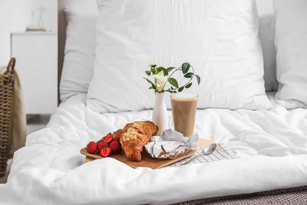 Tray with tasty breakfast, coffee and flowers on white blanket in bedroom - Photo, Image