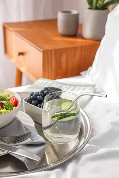 Vassoio con insalata di verdure, mirtilli e bicchiere di acqua di cetriolo su coperta in camera da letto, primo piano - Foto, immagini
