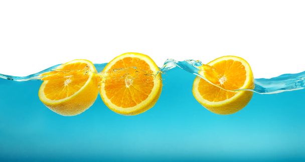 Frutas frescas de color naranja que fluyen en olas de agua azul con salpicaduras aisladas sobre fondo blanco. - Foto, Imagen