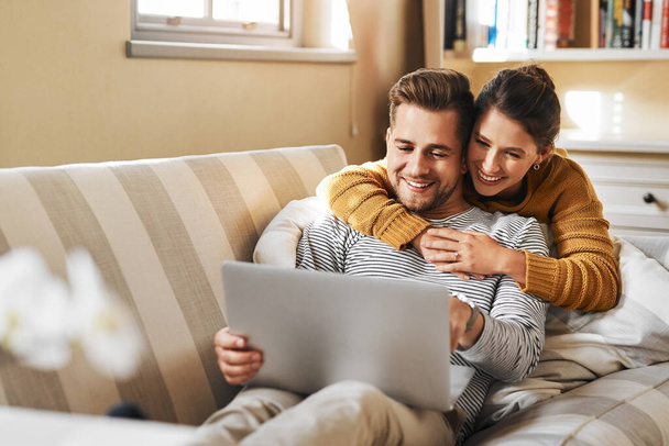 Que lisez-vous ? un jeune couple utilisant un ordinateur portable tout en se relaxant à la maison - Photo, image