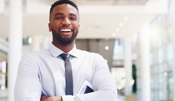 Uśmiech sukcesu. Przycięty portret przystojnego młodego biznesmena stojącego z rękoma złożonymi reklamami trzymającego tablet w biurze - Zdjęcie, obraz