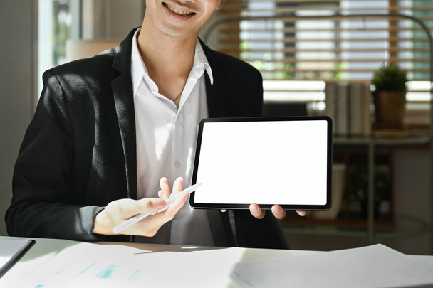 Καλλιεργημένη φωτογραφία του χαμογελαστού επιχειρηματία κρατώντας και δείχνοντας στην ψηφιακή οθόνη tablet. Κενή οθόνη για το διαφημιστικό σας σχέδιο. - Φωτογραφία, εικόνα