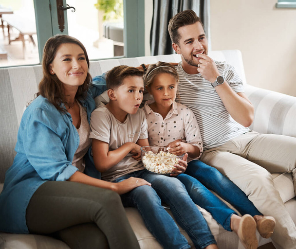 Filme, die die ganze Familie liebt. eine glückliche junge Familie, die es sich auf dem Sofa gemütlich macht und zu Hause gemeinsam fernsieht - Foto, Bild
