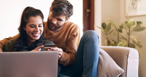 Tule kulta, hemmotellaan itseämme. nuori pari, joka käyttää kannettavaa tietokonetta ja luottokorttia kotona sohvalla - Valokuva, kuva