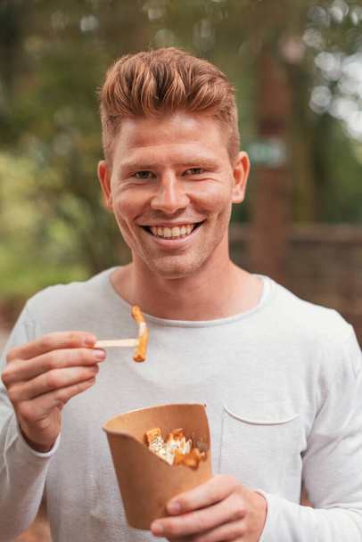 smiling caucasian young man eating french fries - 写真・画像