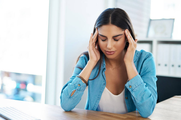 Tension headaches can really put a damper on your day. a young businesswoman looking stressed out while working in an office - Foto, Bild