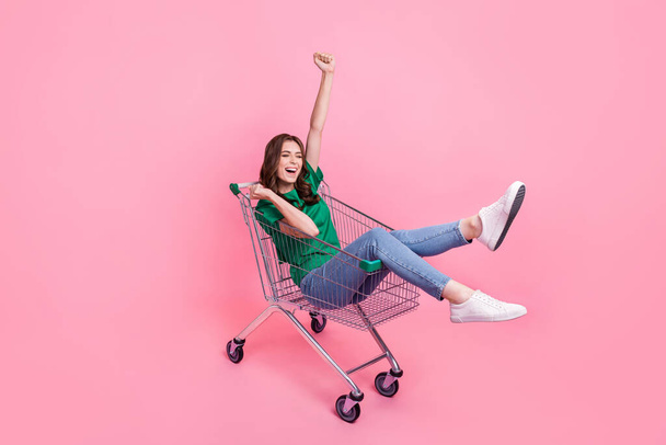 Full length photo of overjoyed lady stylish clothes sit cart raise hand fist eyes closed celebrate sale isolated on pink color background. - 写真・画像