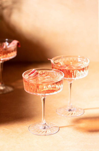 Коктейль из ревеня с джином и тоником, вид спереди на стаканы с алкогольным коктейлем, украшенный ревеневыми полосками, готовый к употреблению - Фото, изображение