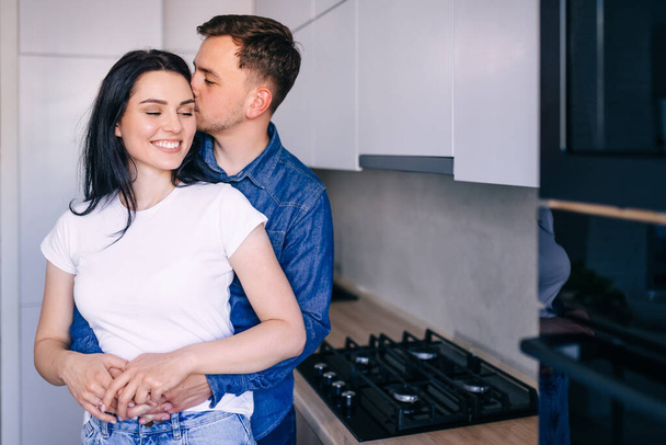 Atraktivní mladá žena a pohledný muž rádi tráví čas spolu, stojí v jasné moderní kuchyni. - Fotografie, Obrázek