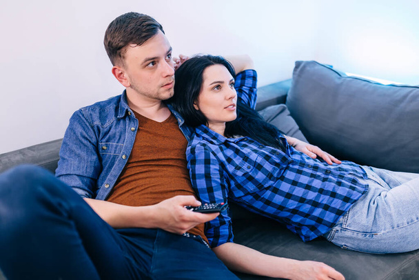 junges ernsthaftes Paar liegt auf der Couch und schaut die Nachrichten im Fernsehen. - Foto, Bild