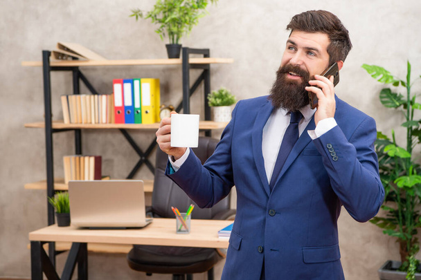 How can I help you. Happy manager talking on phone drinking tea. Business call. Phone call at work. Mobile communication. Working in office. - 写真・画像