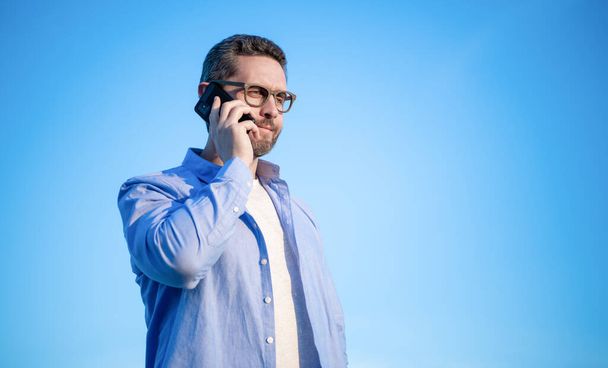 communication of man in glasses talk on phone. man talking on phone. man communication talk on sky background. copy space. - Foto, imagen