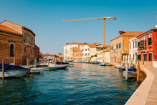 Murano, Włochy - październik 2022: Kanał Murano z kolorowymi domami, zacumowanymi łodziami i dźwigami w tle - Zdjęcie, obraz