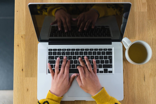 Laptopuyla çalışan bir kadın, yanında bir kupa çayla ve tahta bir masanın üstünde siyah ekranla. Yüksek kalite fotoğraf - Fotoğraf, Görsel