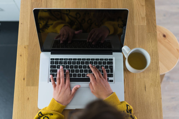 Laptopuyla çalışan bir kadın, yanında bir kupa çayla ve tahta bir masanın üstünde siyah ekranla. Yüksek kalite fotoğraf - Fotoğraf, Görsel