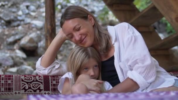 Happy cute affectionate a mother hugs a little upset daughter. A loving woman comforts a sad little girl in a restaurant in the summer. Family travel. High quality FullHD footage - Footage, Video