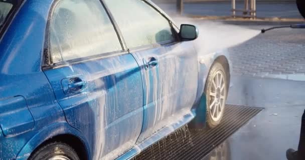 Közelkép a modern jármű mosott névtelen személy nagy nyomású vízzel. Egy nagyon koszos autót tiszta vízzel tisztítanak meg. - Felvétel, videó