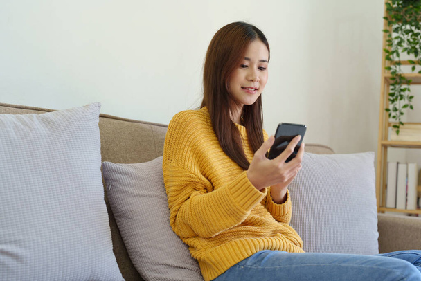 woman sitting on sofa at home ready to use mobile phone. - Foto, Bild
