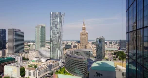 Varsó központja a Kultúra és Tudomány Palotájával. A városközpont légi felvételei felfelé repülnek egy üveghomlokzattal az előtérben. A nyári szezon napos napja a városban. - Felvétel, videó