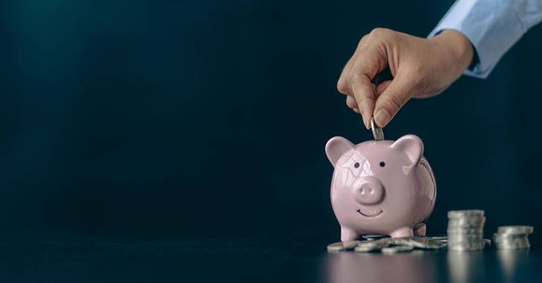 青い背景にピンクの豚貯金箱と女性の手のコイン。テキストのためのスペースをコピーする黒い背景に貯金箱にコインを入れます。将来の投資アイデアのためにお金を節約. - 写真・画像