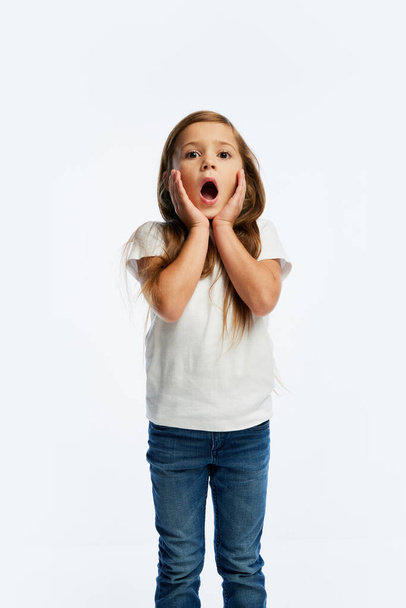 Wow, surprise. Excited elementary school age girl, pupil in casual style clothes isolated over white background. Concept of children emotions, fashion, facial expressions. Copy space for ad - 写真・画像